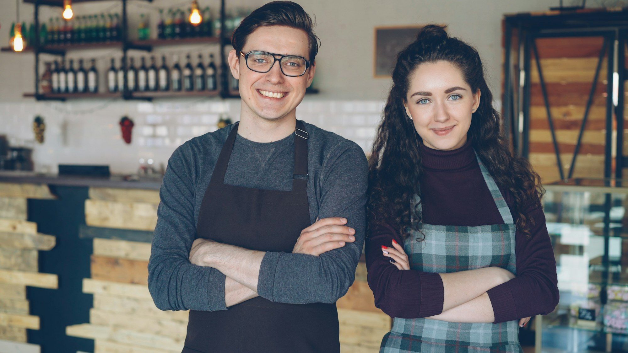 Deux gérants de café, bras croisés, souriants devant leur comptoir